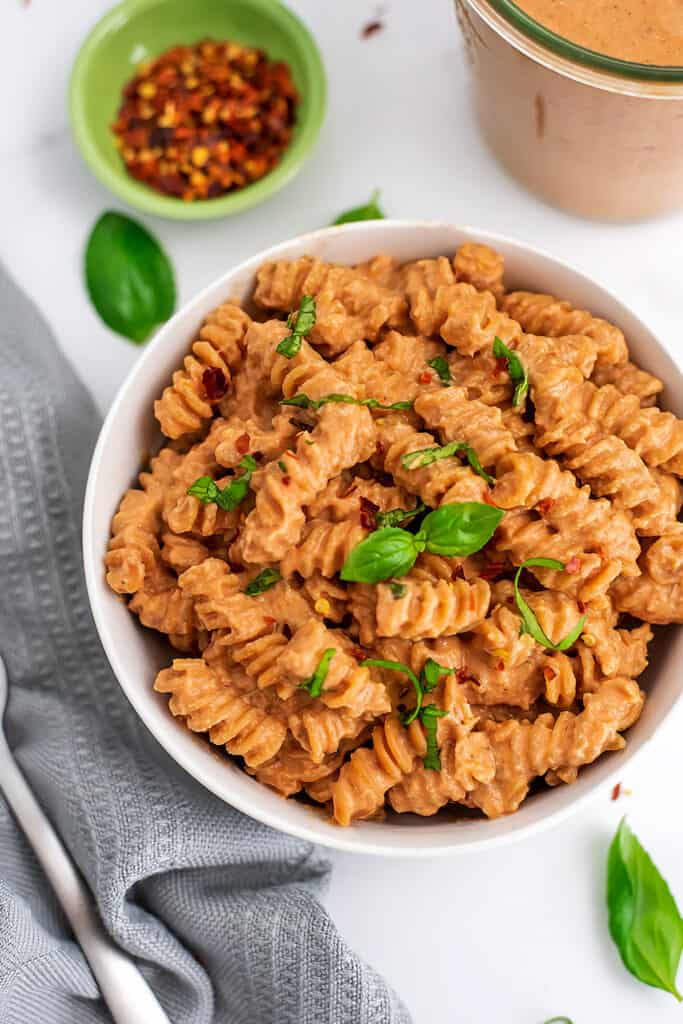 Creamy tomato pasta in a white bowl topped with basil.