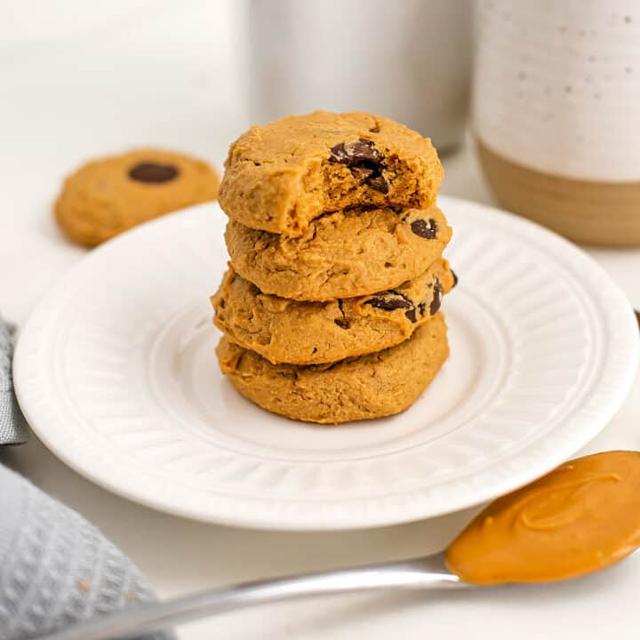 Four peanut butter cookies stacked on white plate, one with bite taken.