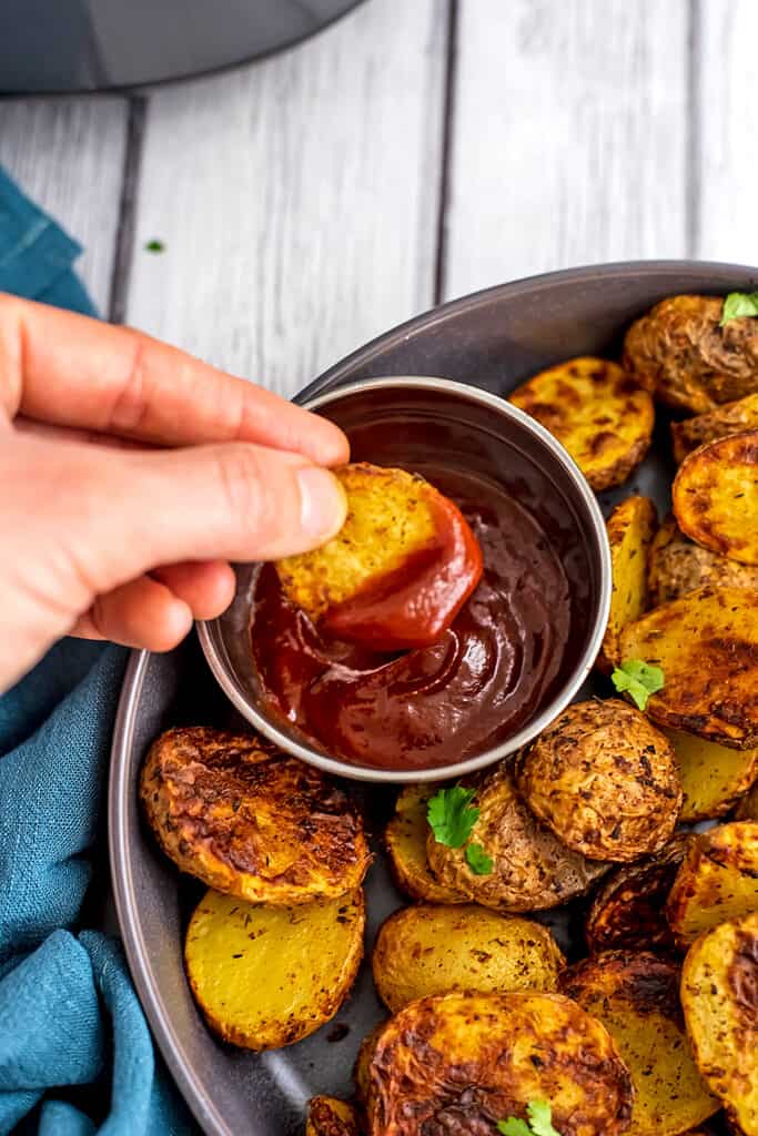 Hand dipping potatoes in ketchup.