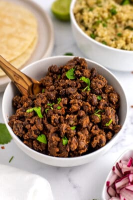 White bowl filled with mexican black beans with wooden spoon.