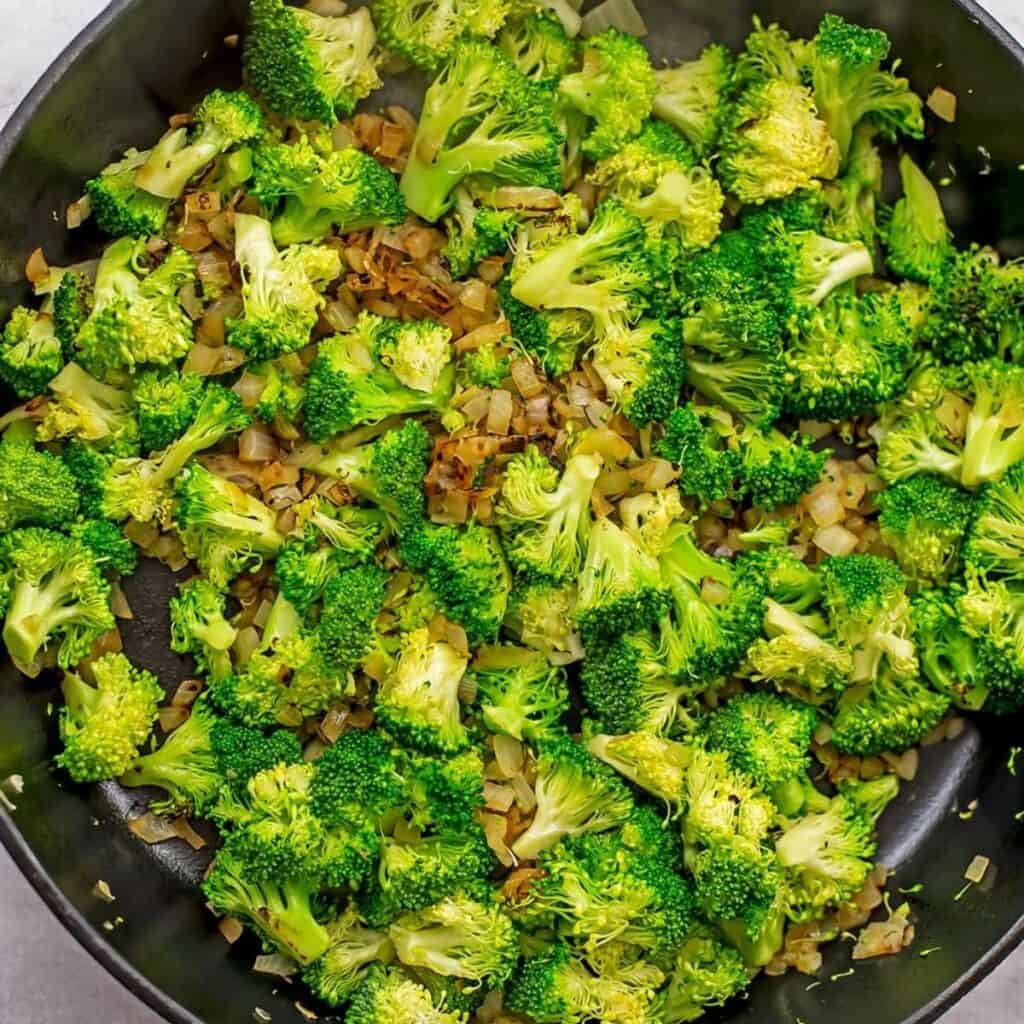 Skillet filled with broccoli and cooked onions.