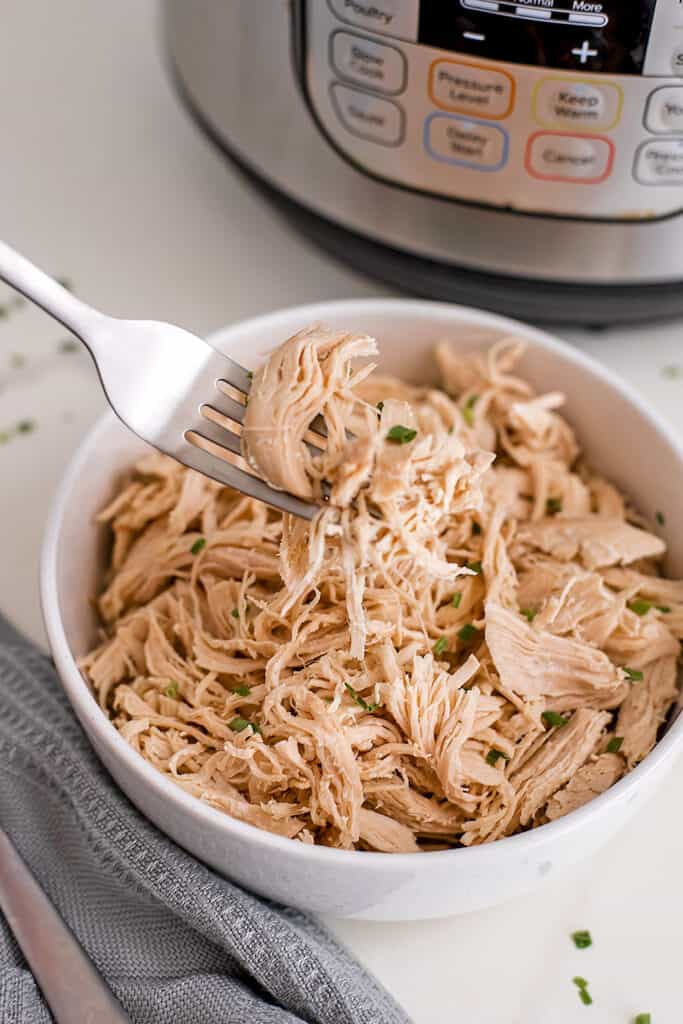 Shredded chicken on a fork over a bowl of chicken.