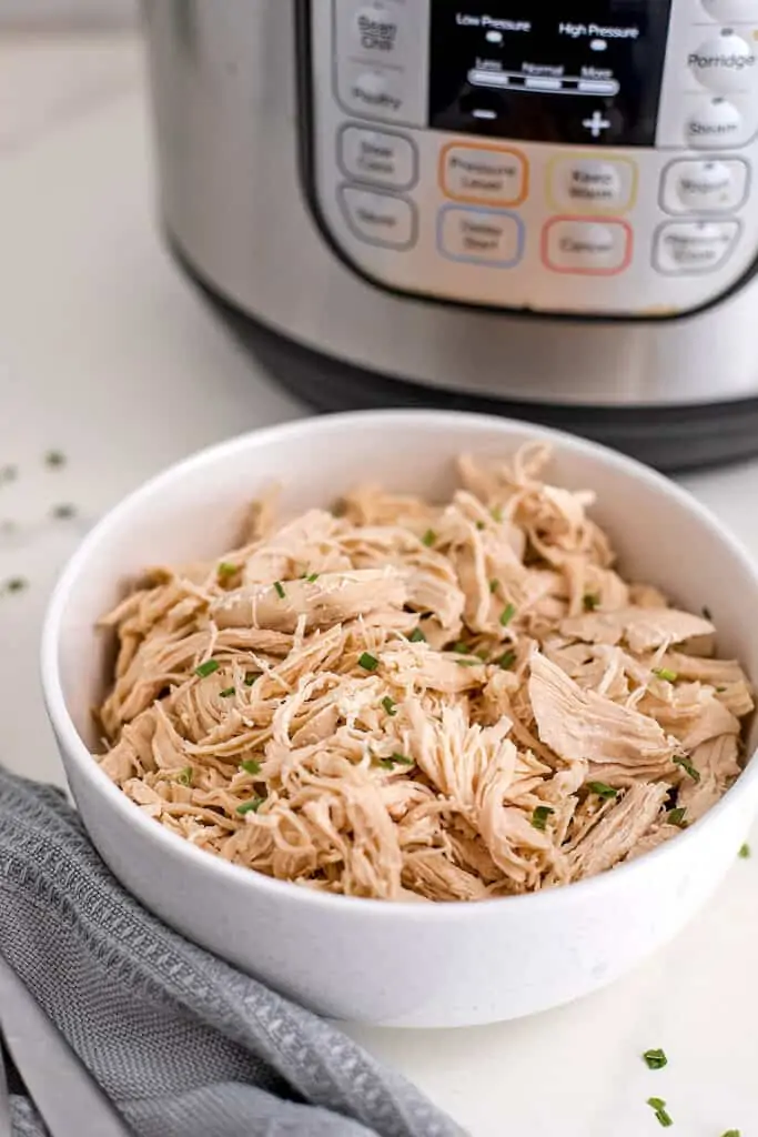 White bowl filled with shredded chicken, instant pot in background.