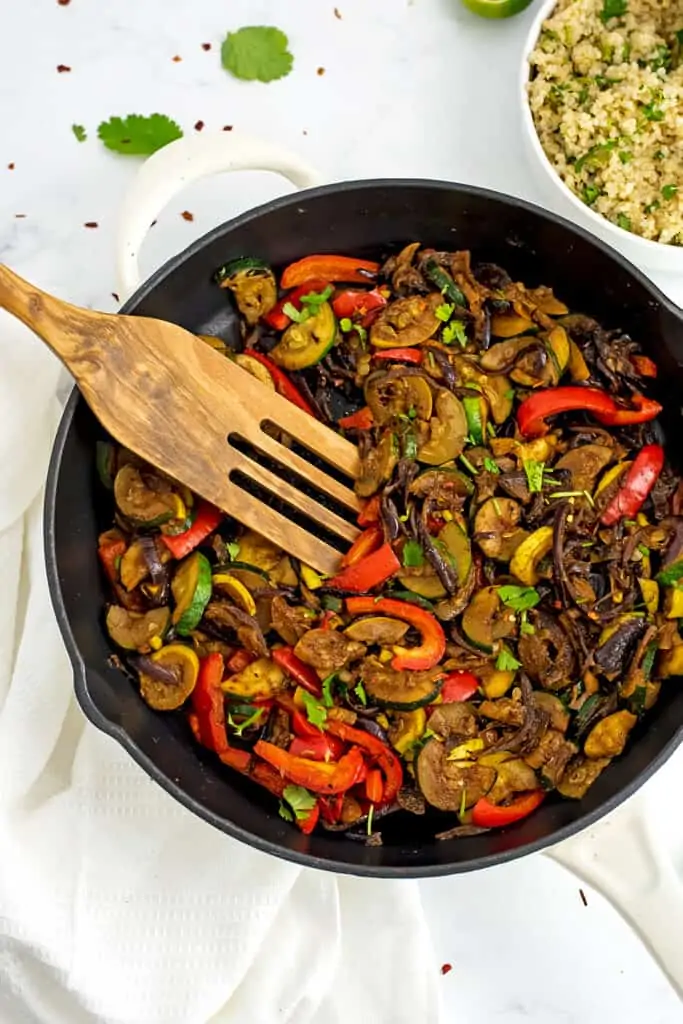Wooden spatula in cast iron full of Mexican stir fry vegetables.
