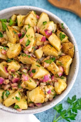 Parsley potato salad in white bowl with parsley on the side.