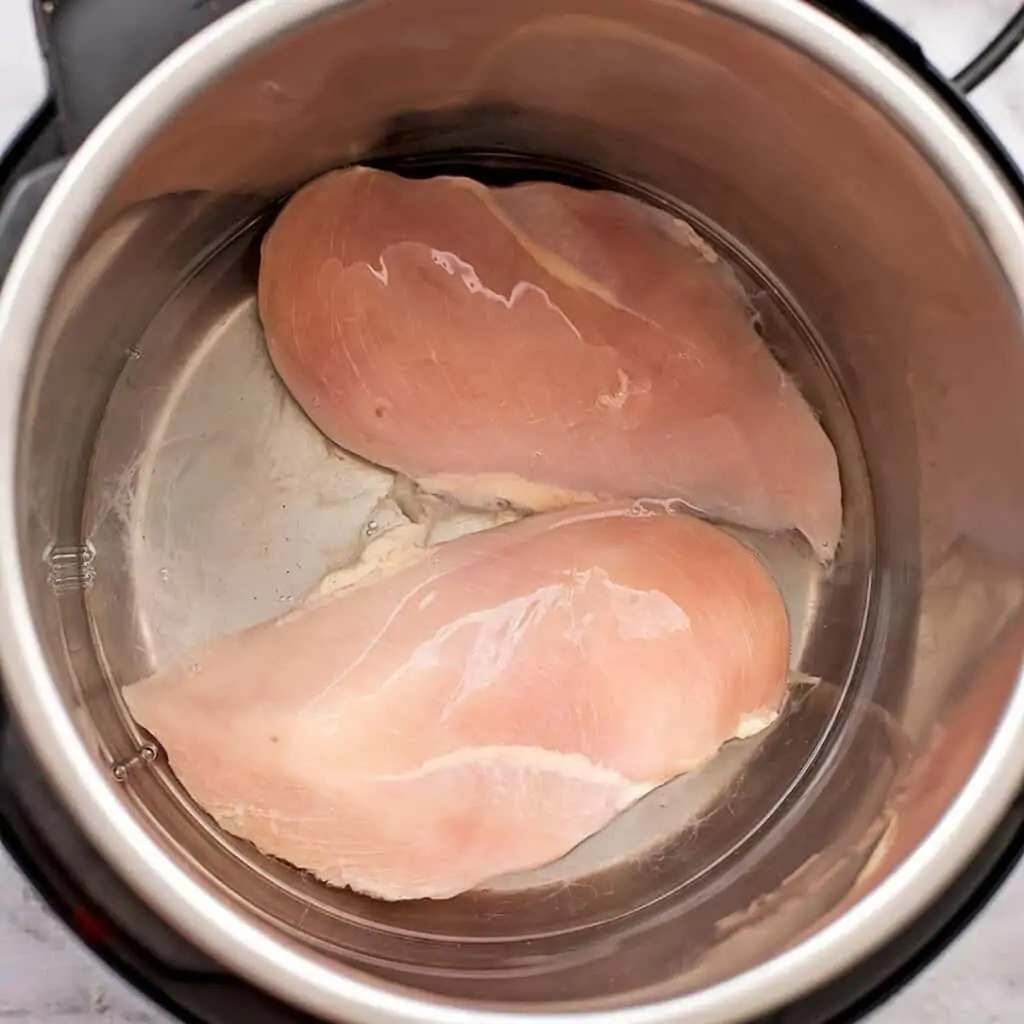 Fresh chicken breast in instant pot with water before cooking.
