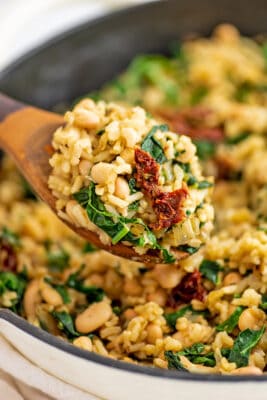 Large wooden spoonful of tuscan white bean skillet from the cast iron skillet.