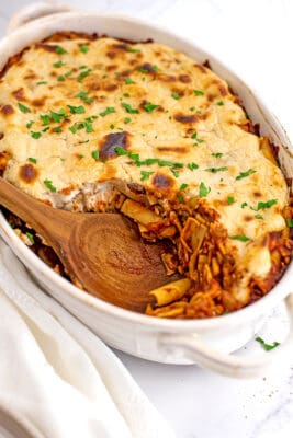 Wooden spoon in casserole dish of vegetarian baked ziti.