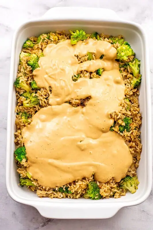 Dairy free cheese sauce poured over a casserole dish filled with broccoli and rice.