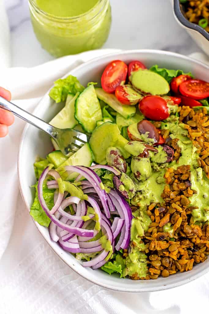 Fork in a bowl filled with vegan shawarma topped with cilantro tahini dressing.