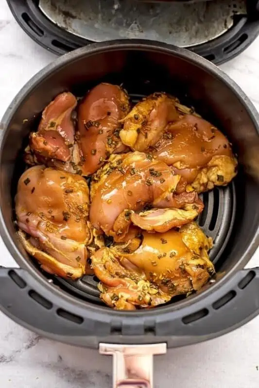 Air fryer basket filled with teriyaki chicken thighs before cooking.