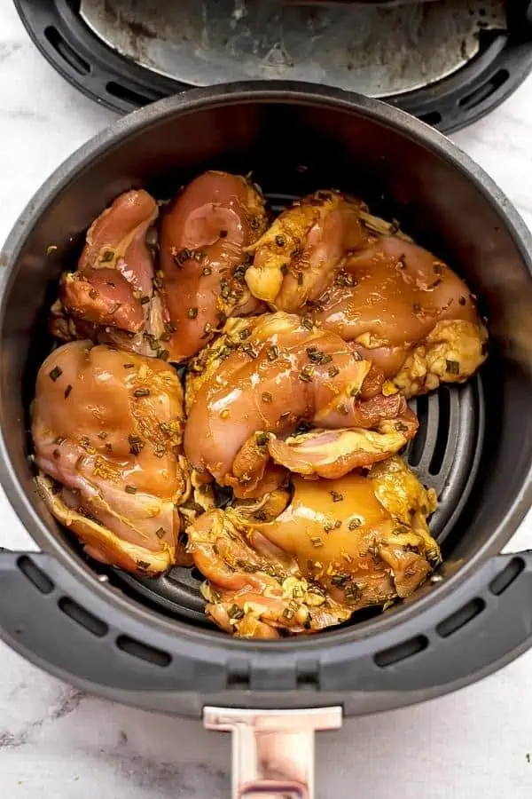 Air fryer basket filled with teriyaki chicken thighs before cooking.