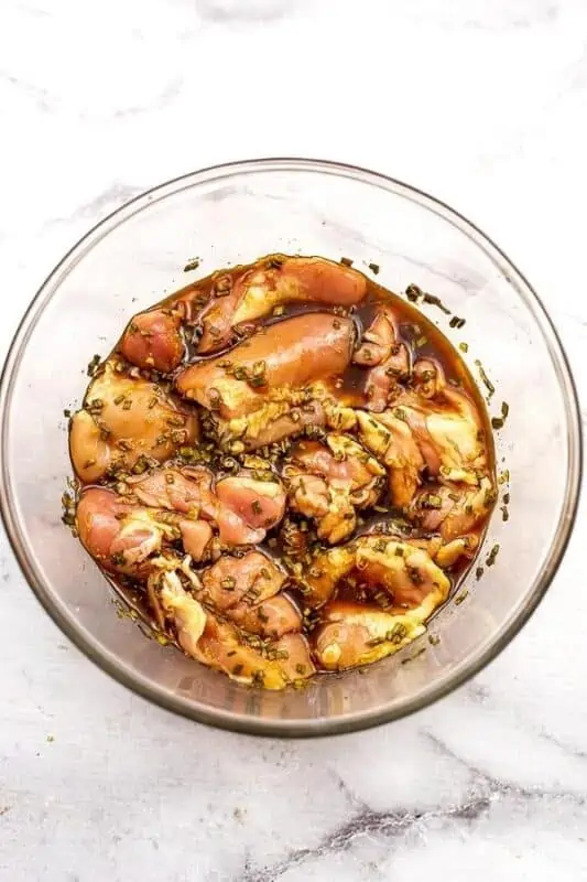 Chicken thighs in teriyaki marinade in glass bowl.