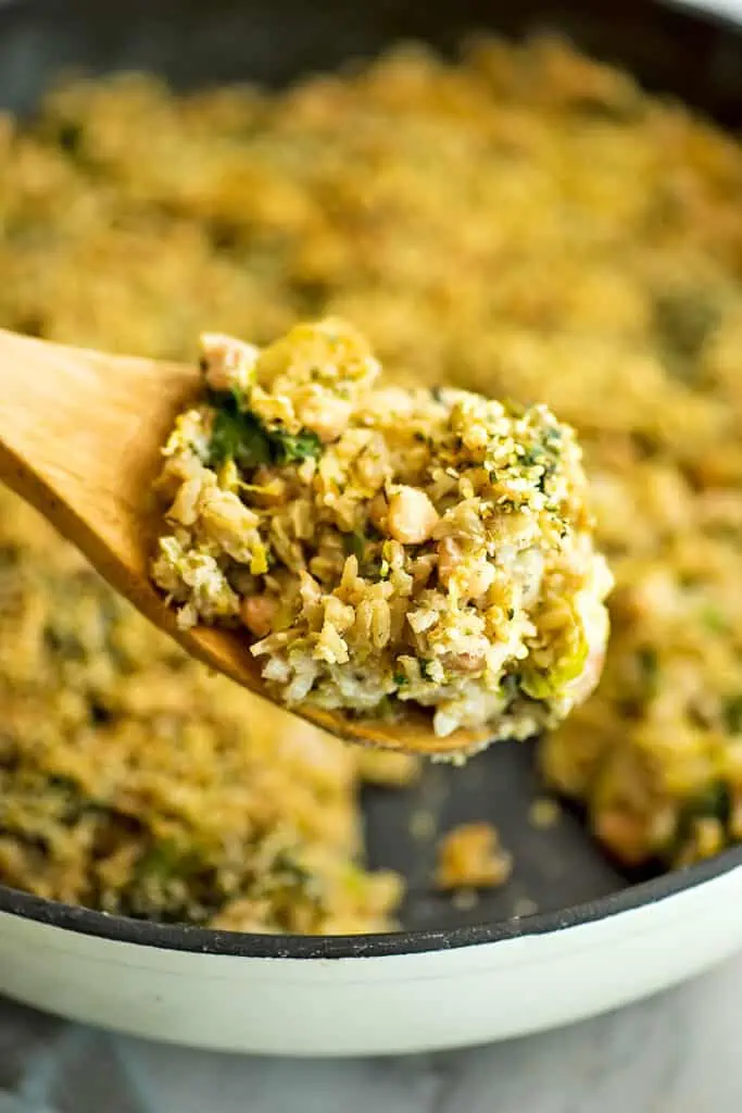 Vegan brussel sprouts casserole in skillet, with a wooden spoonful of casserole.