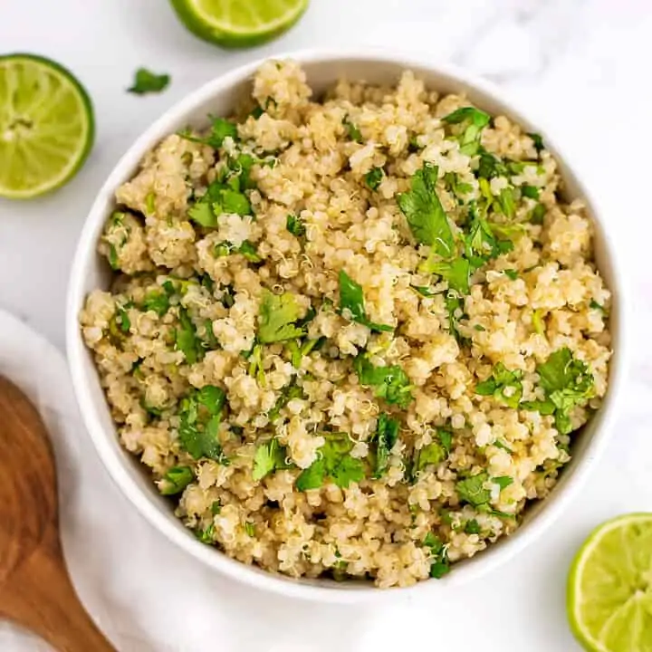 Cilantro lime quinoa in a white bowl with limes around the bowl.