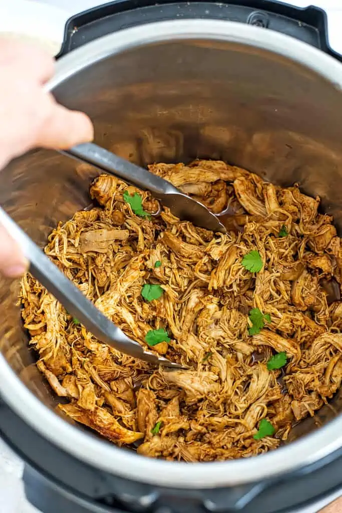 Tongs being held over a pot of instant pot Mexican shredded chicken.
