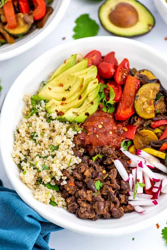 Quinoa, black beans, veggies and avocado in a white bowl.