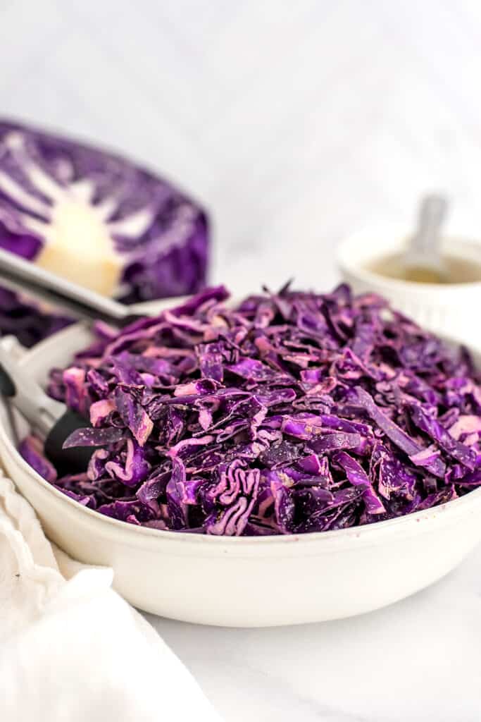 White bowl filled with vegan red cabbage slaw, tongs in the bowl.
