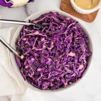 White bowl filled with red cabbage slaw and tongs.