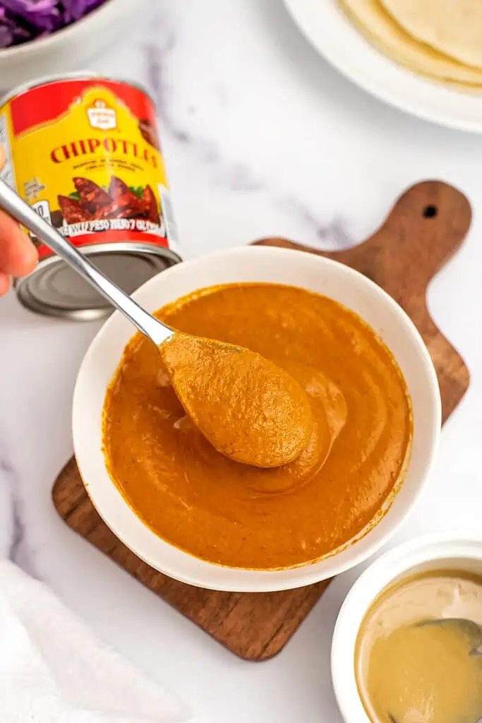 Chipotle tahini dressing in white bowl, spoonful of sauce over the bowl.