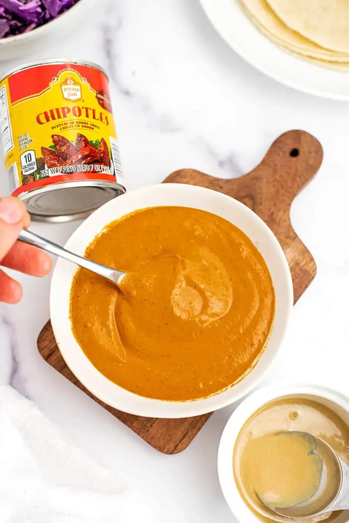 Hand holding a spoon in a bowl of spicy tahini dressing.