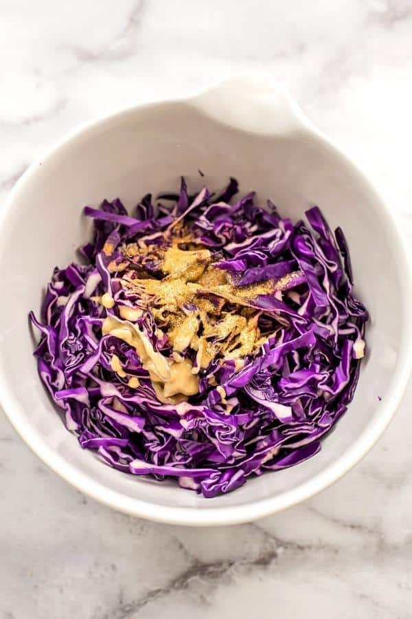 Red cabbage, tahini, spices in a white bowl before mixing.