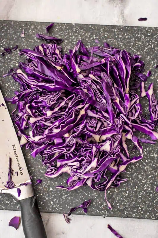 Red cabbage thinly sliced on a cutting board.