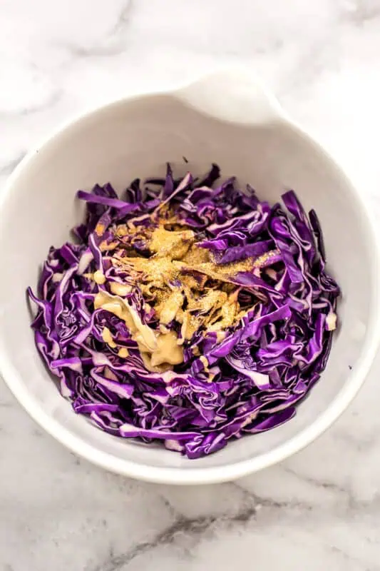 Red cabbage in bowl with tahini and spices before stirring.