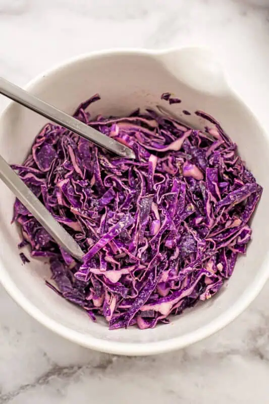 Tongs resting in a bowl of red cabbage coleslaw.