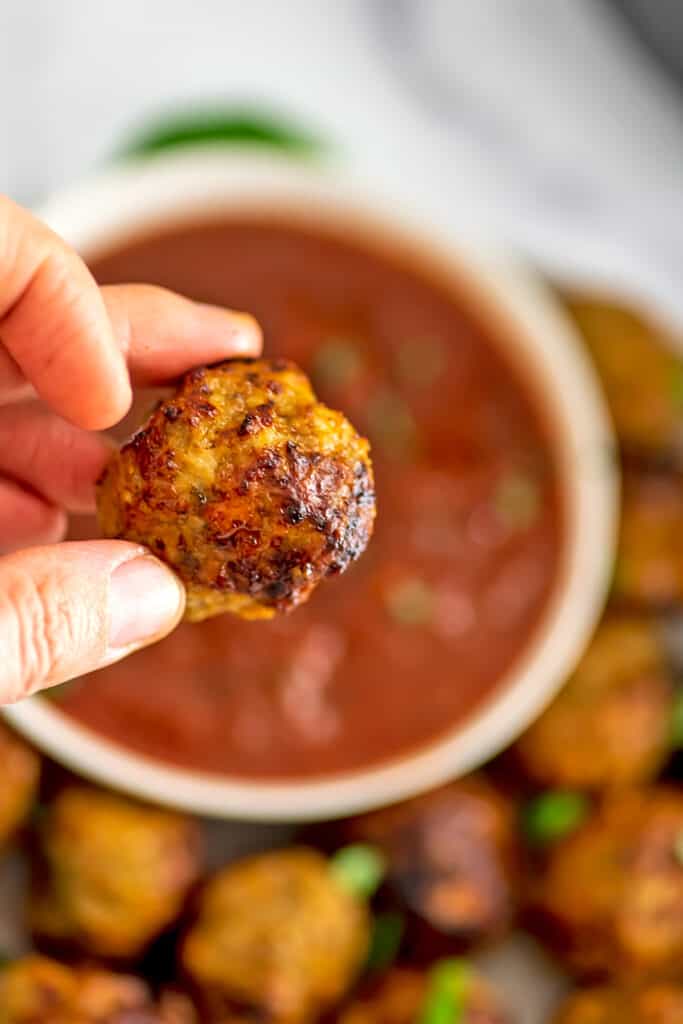 Hand holding a chicken meatball that has been dipped in marinara sauce.