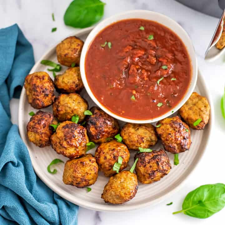 White plate filled with air fryer chicken meatballs and a bowl of marinara.