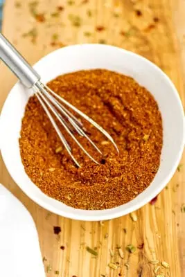 White bowl filled with homemade cajun seasoning with a small whisk in bowl.
