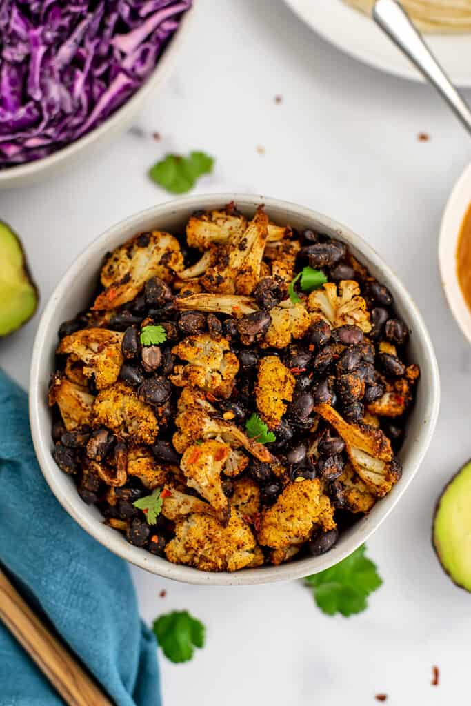White bowl filled with spiced cauliflower and black beans.