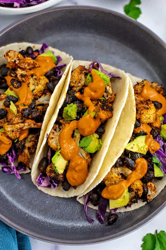 Vegan cauliflower tacos with spicy tahini sauce on grey plate. 