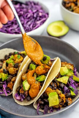 Spicy tahini sauce being drizzled over cauliflower black bean tacos.