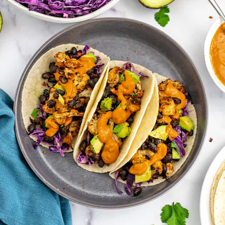Three cauliflower black bean tacos on a great plate with blue napkin.