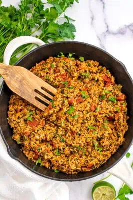 Large skillet filled with chimichurri rice with large wooden spatula.