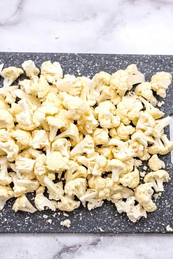 Chopped cauliflower florets on a grey cutting board.