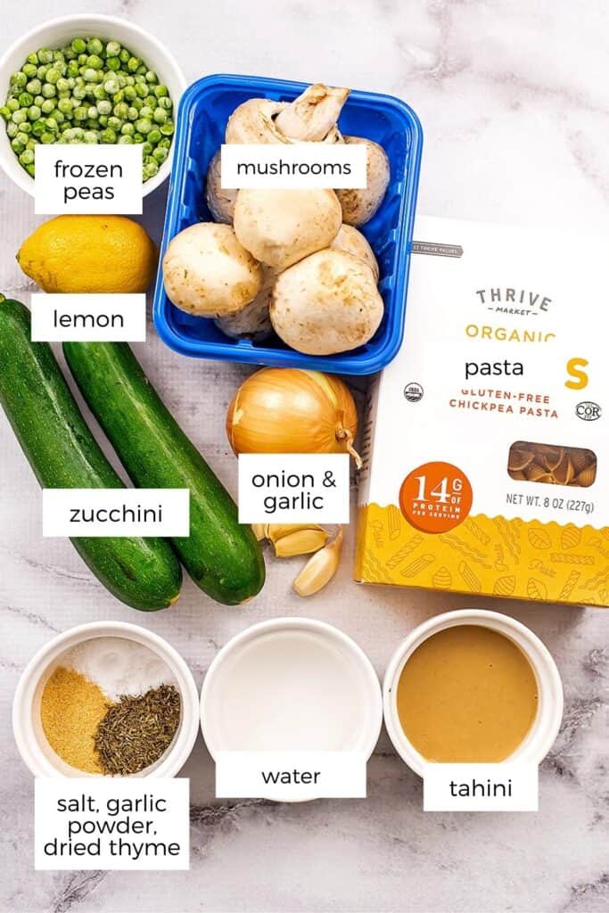 Ingredients to make mushroom zucchini pasta in ramekins on marble surface.