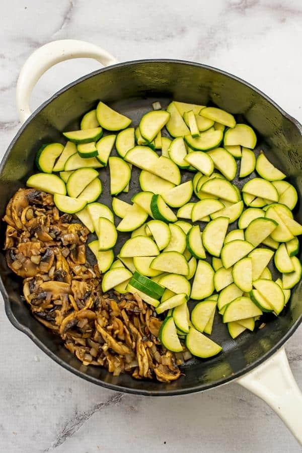 Cast iron skillet with zucchini added, cooked mushrooms pushed to the left side.
