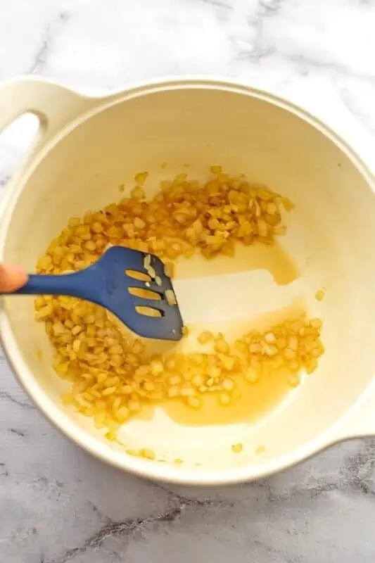 Cooked onions in a white pot, spatula scraping the pot.