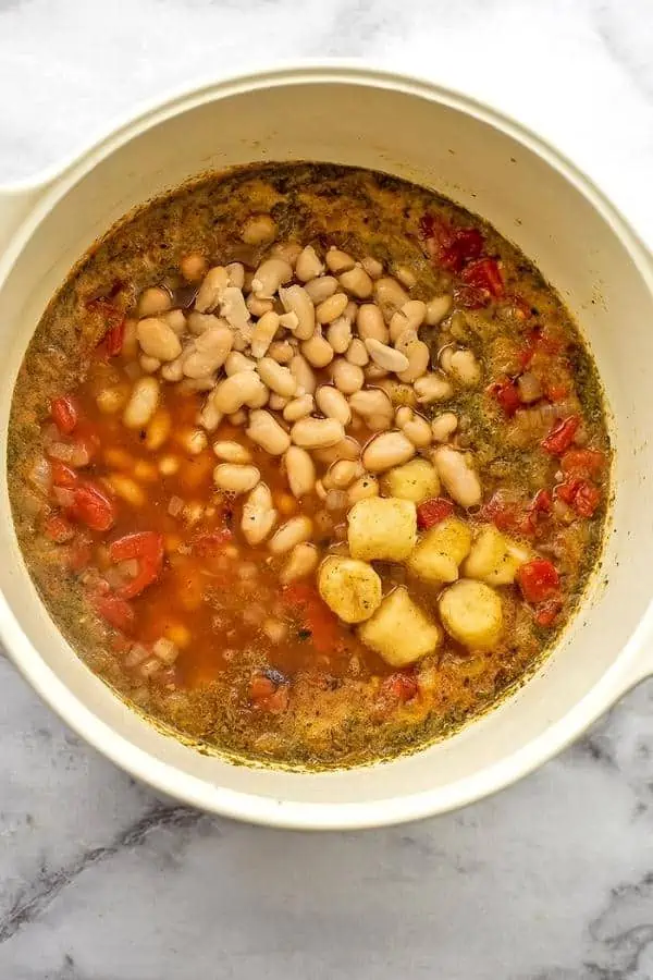 White beans and gnocchi in tomato based soup in a pot.