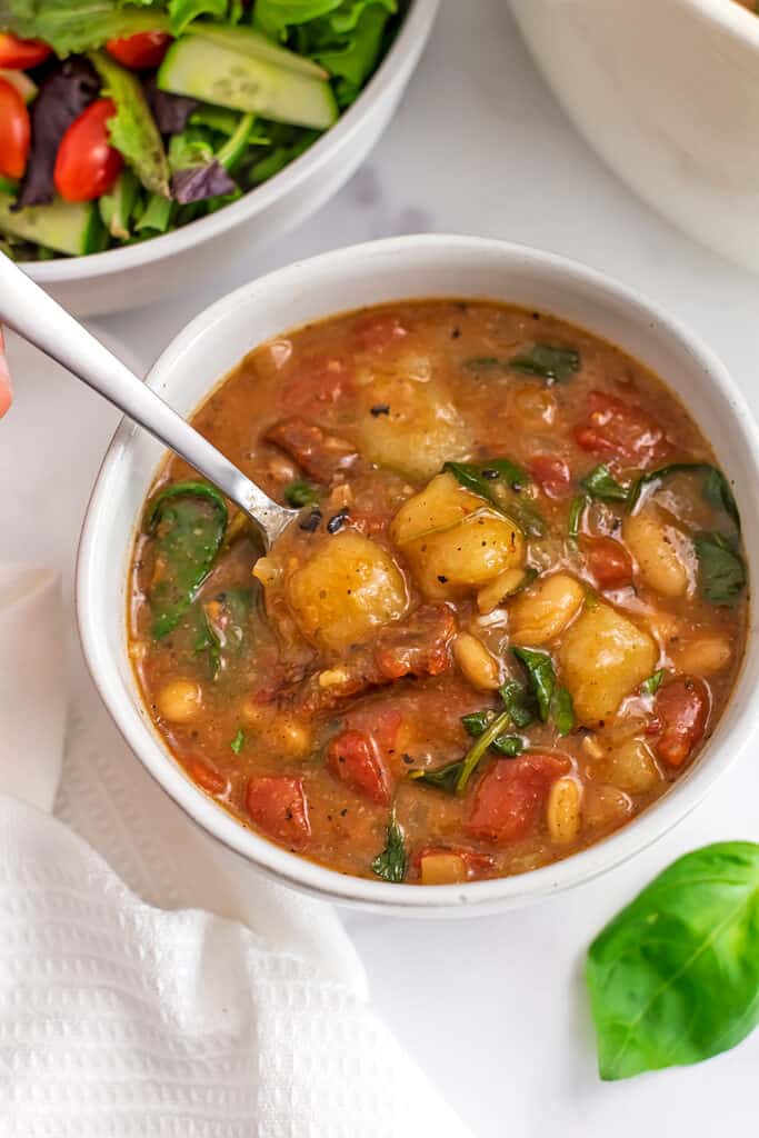 Tomato gnocchi soup in a white bowl with spoon in the bowl.