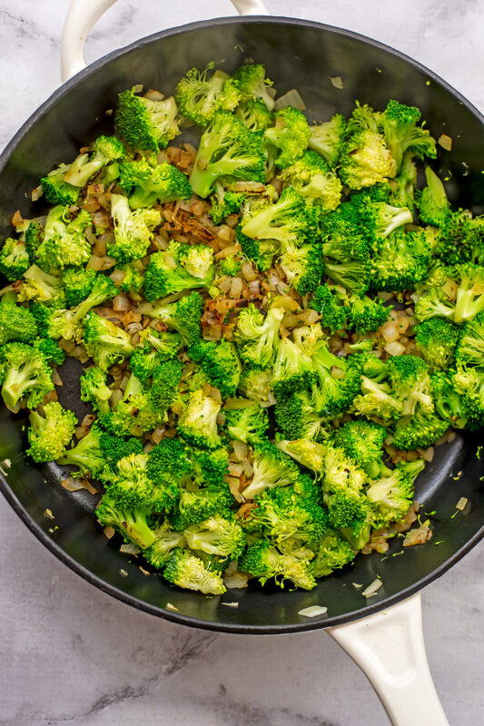 Broccoli florets added to cast iron skillet with onions.