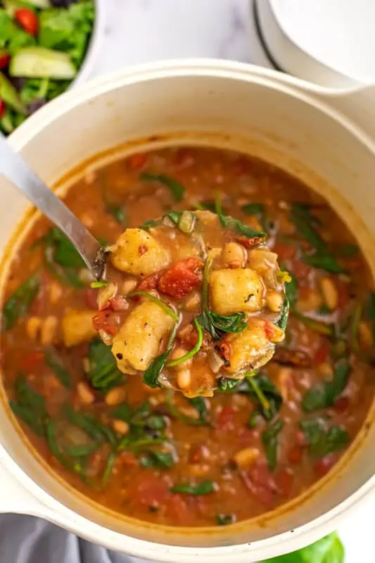 Vegan gnocchi soup in a large white pot, ladle in the pot.