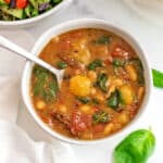 Vegan tomato gnocchi soup in white bowl with basil around the bowl.