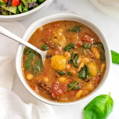 Vegan tomato gnocchi soup in white bowl with basil around the bowl.