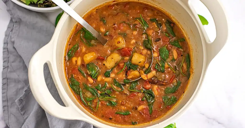 Sliver spoon in large pot filled with vegan gnocchi soup.