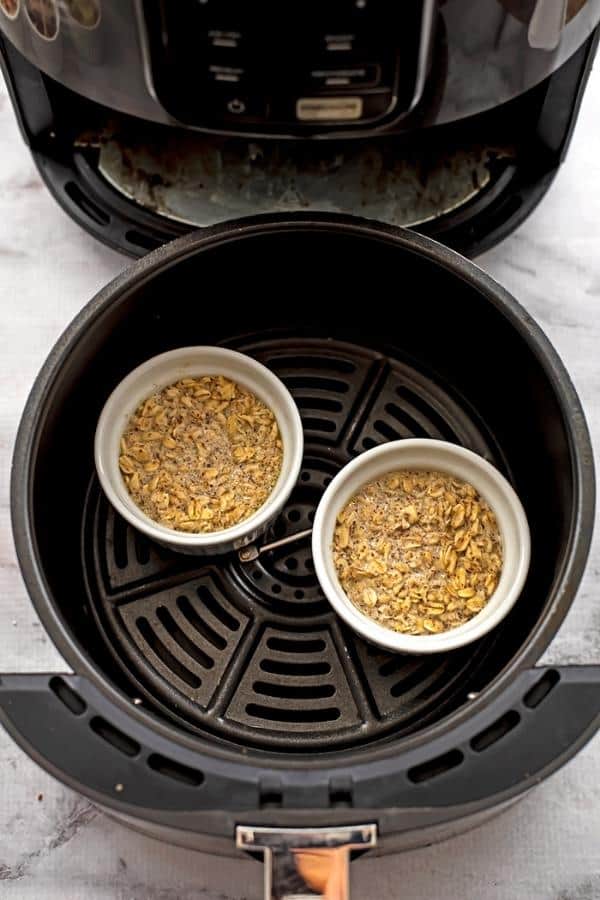 Oatmeal in ramekins in air fryer basket before baking.