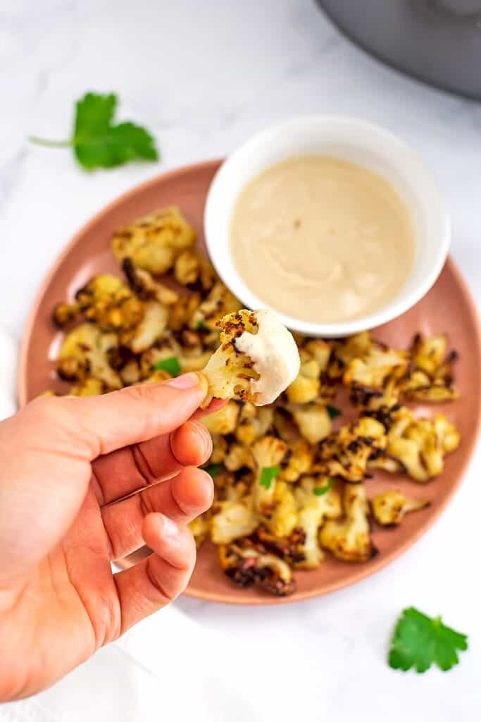 Hand holding piece of cauliflower dipped in tahini ranch.